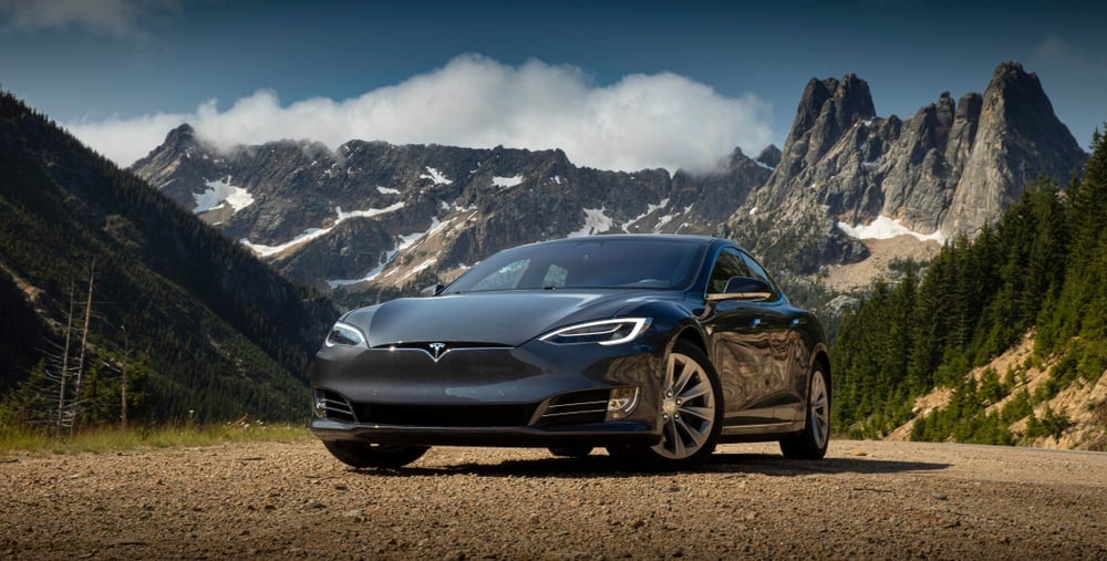 Tesla model 3 parked against a backdrop of a rocky mountain.