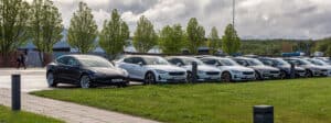 six Polestar 2 electric cars and a Tesla 3 at a parking lot.