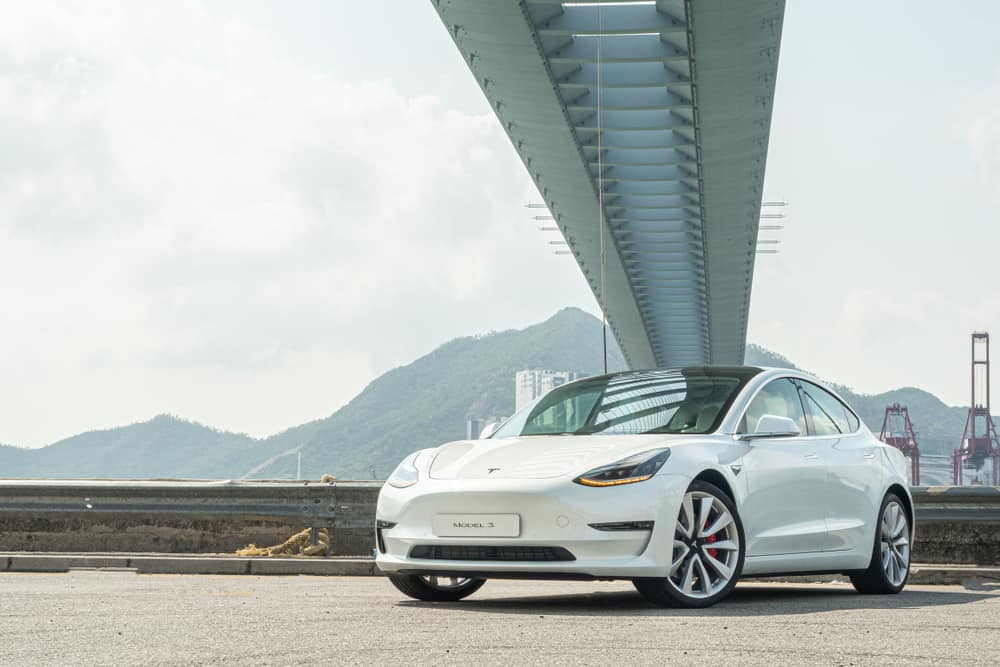 white Tesla Model 3 parked under a bridge