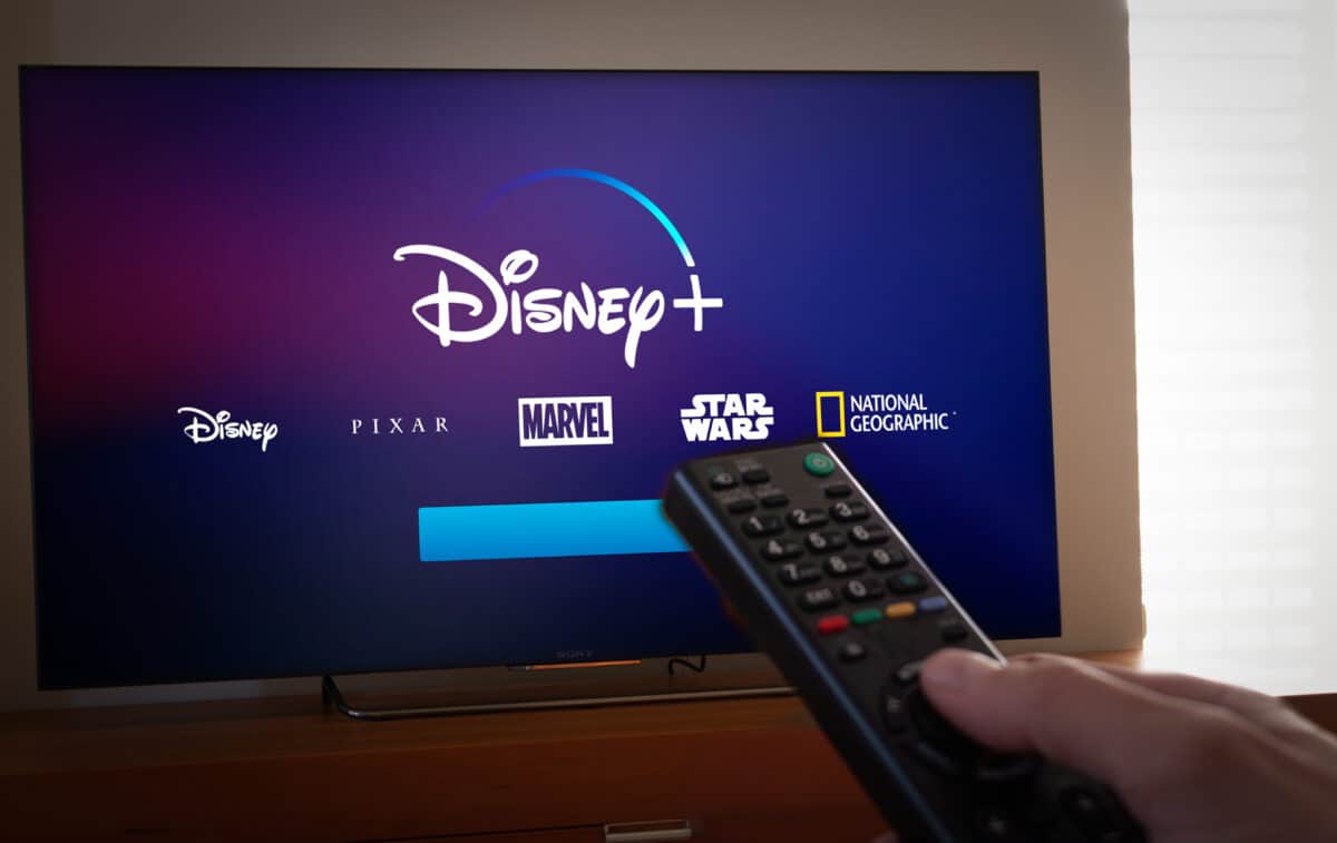 Man points a remote control to a TV screen with Disney+