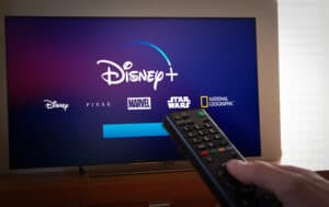 Man points a remote control to a TV screen with Disney+
