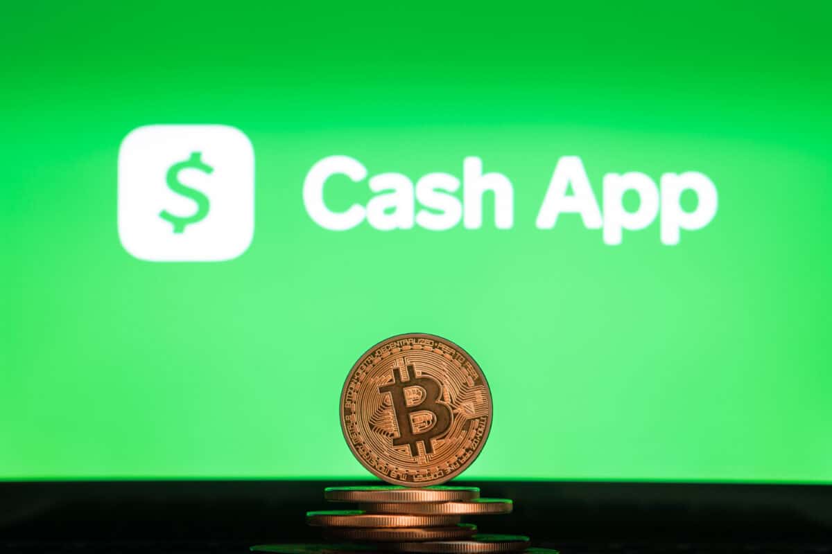 A stack of bitcoin in front of the Cash App logo.
