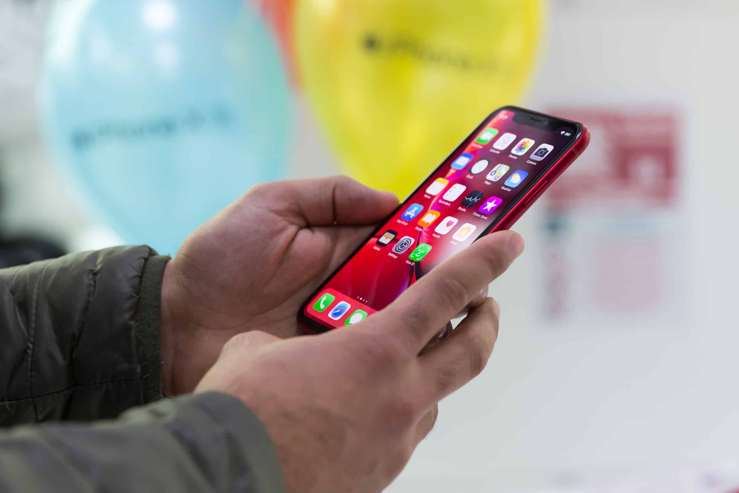 hands holding a red iPhone XR with the homescreen displayed.