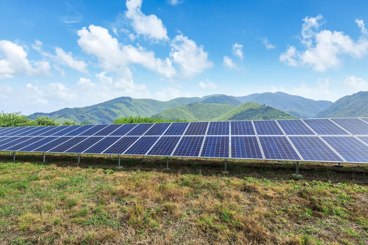This image portays a solar panel array in a field with mountains in the background.