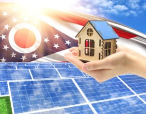 The photo with solar panels and a woman's palm holding a toy house shows the flag State of Ohio in the sun.