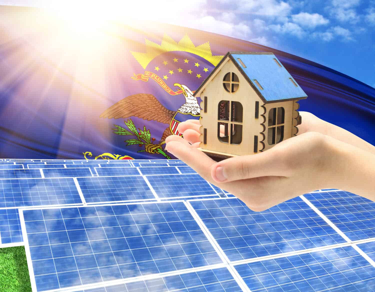 The photo with solar panels and a woman's palm holding a toy house shows the flag State of North Dakota in the sun.