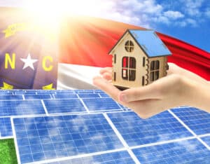 The photo with solar panels and a woman's palm holding a toy house shows the flag State of North Carolina in the sun.