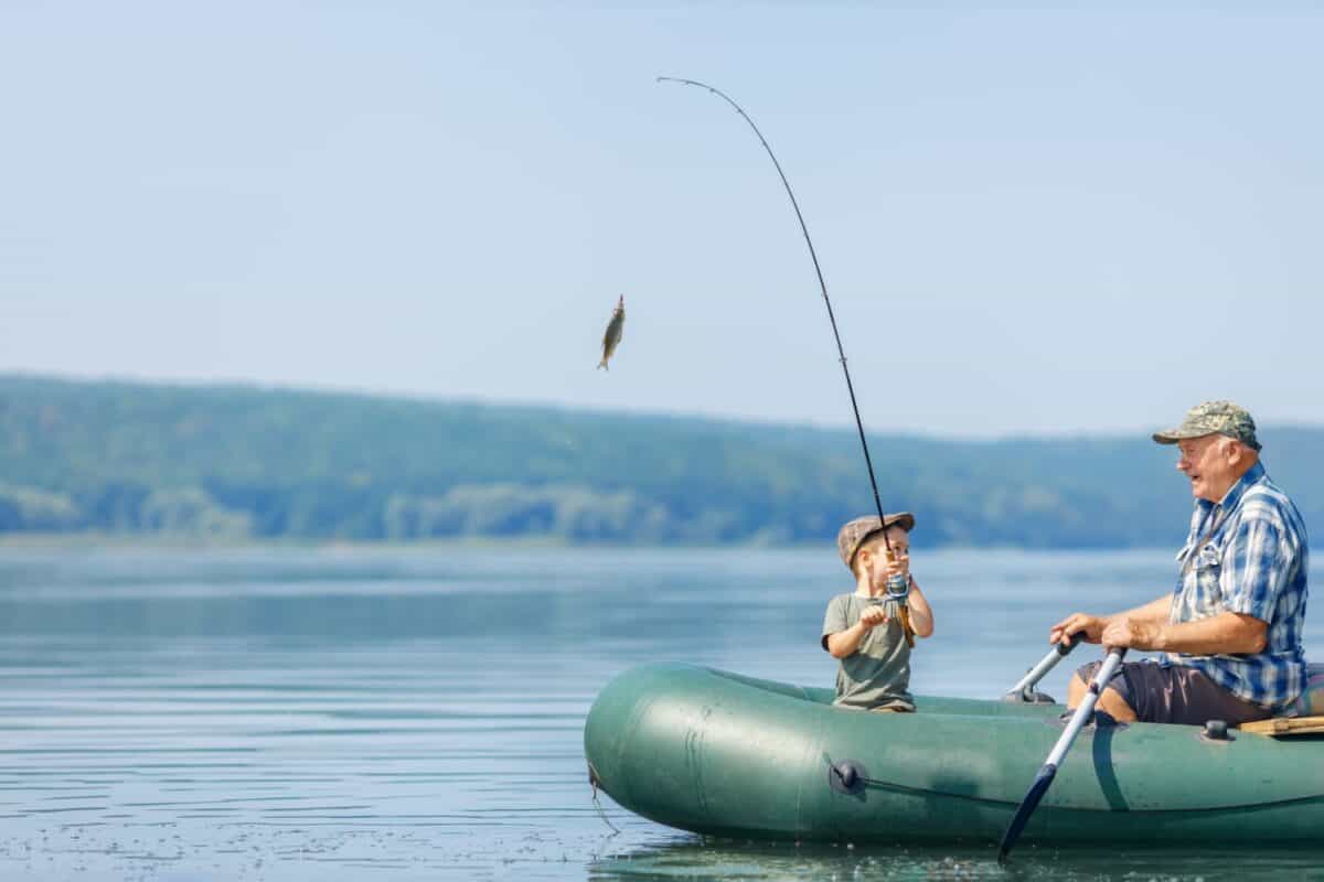 grandfather with grandson together fishing from inflatable boat. Little boy caught fish. Concept of connection between generations