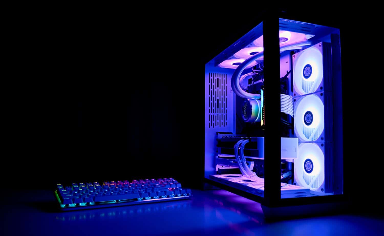 Water Cooled Gaming Pc with RGB rainbow LED lighting. Modern gaming computer with a keyboard in a dark room. Water Liquid Cooling Computer