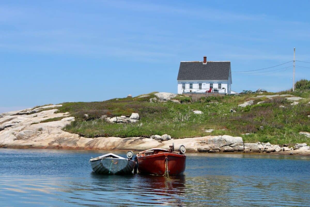 Small cove with a white house on the hill and two colorful johnboats anchored off the rocky shoreline in cool blue water