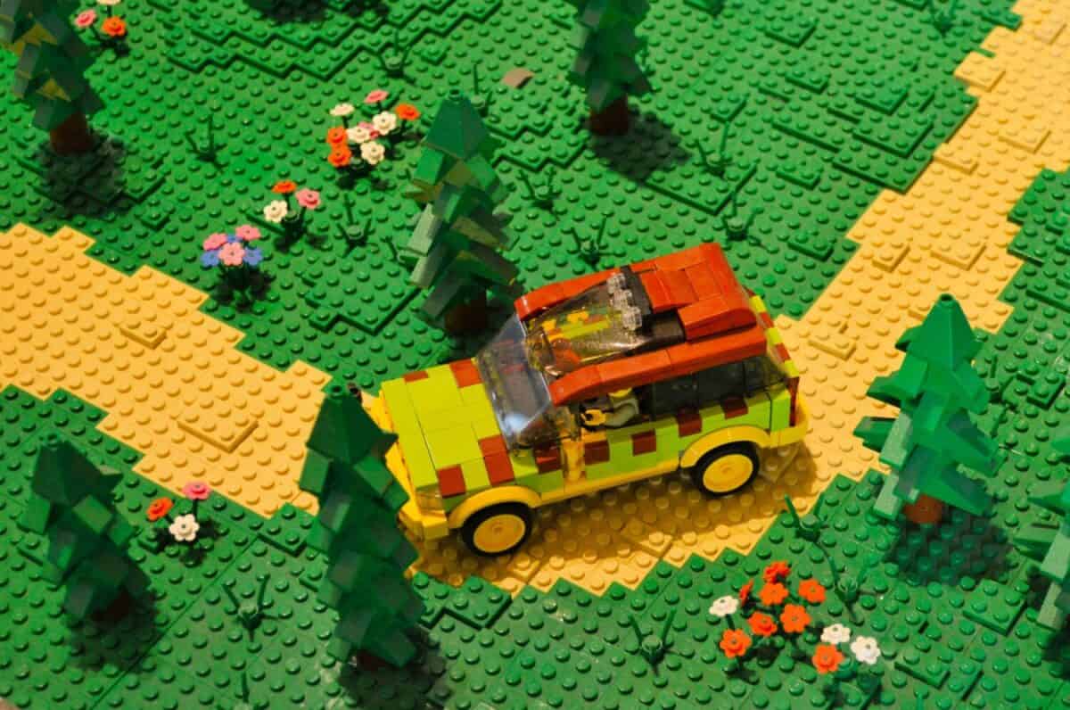 an SUV driving off road on a forest trail surrounded by trees and flowers, made using LEGO toy blocks