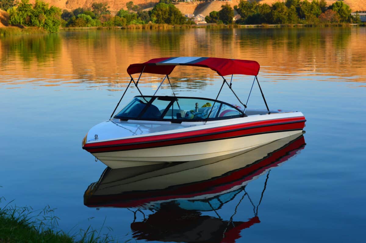 A small outboard runabout boat with canopy lies at anchor on a placid lake.
