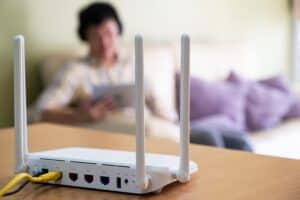 Selective focus at router. Internet router on working table with blurred man using tablet at the background. Fast and high speed internet connection from fiber line with LAN cable connection.