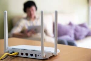 Selective focus at router. Internet router on working table with blurred man using tablet at the background. Fast and high speed internet connection from fiber line with LAN cable connection.