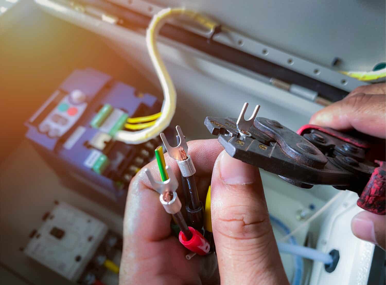Close up, electrician using pliers to crimp terminals on wires. Wiring work, control cabinet, inverter system used to control electric motors.