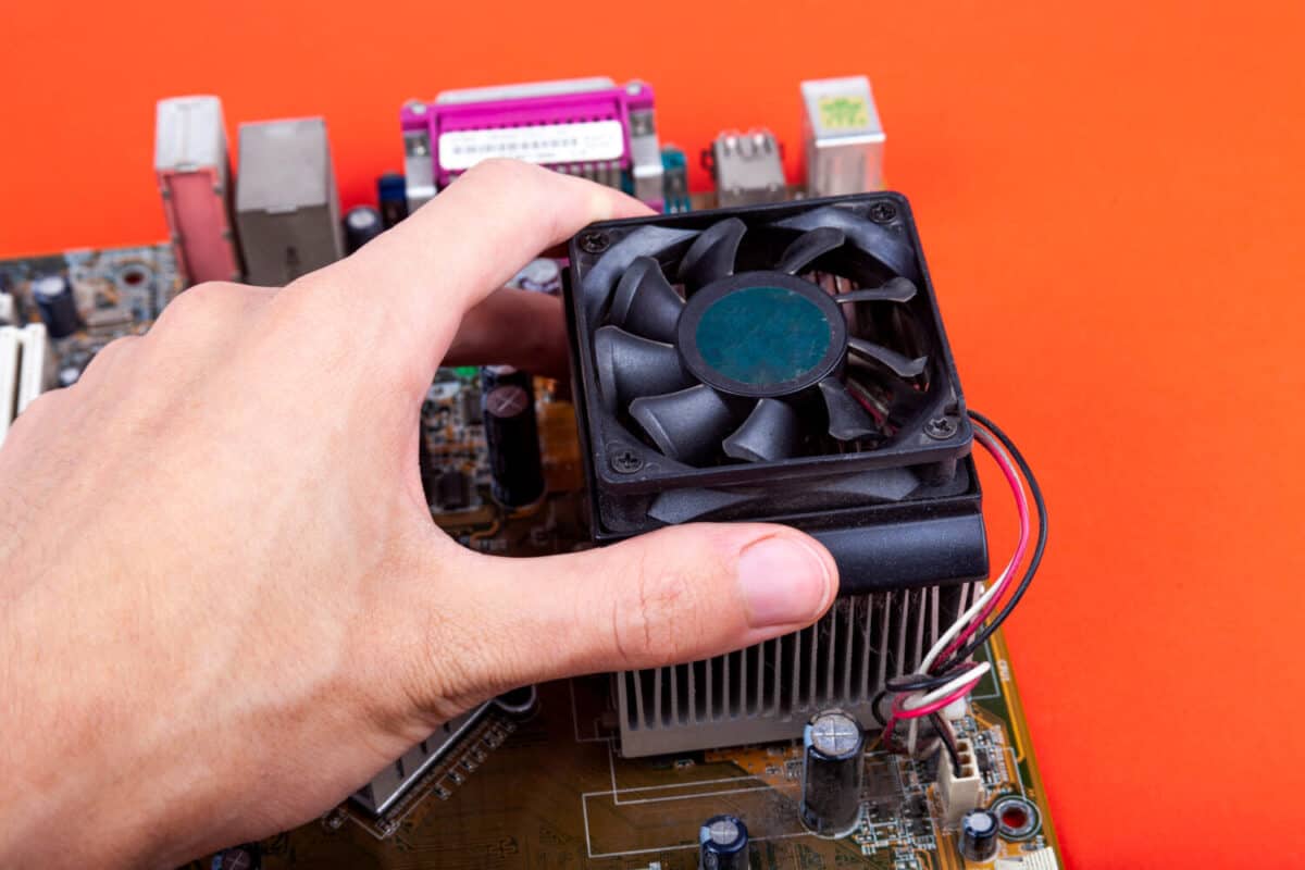 Removing an small old CPU cooler from the motherboard. Human hand dismounting an outdated dusty fan, upgrading processor cooling. PC computer heat problems technology abstract concept isolated on red