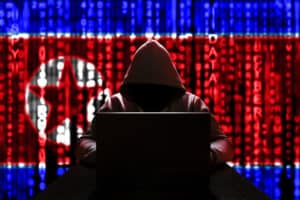 Shadowy silhouette of a North Korean hacker at the computer on a background of binary code set against the flag of the DPRK
