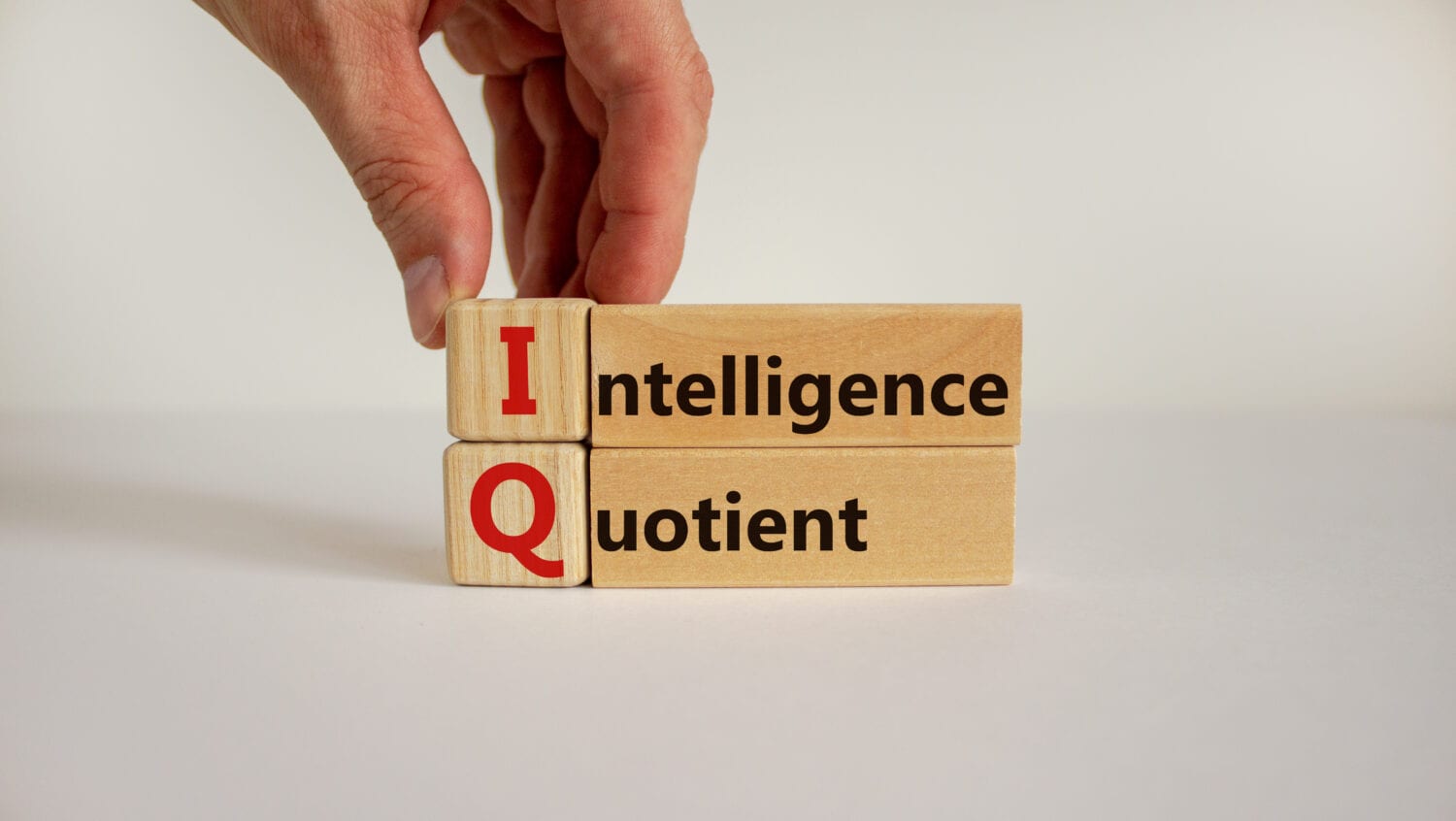 Intelligence quotient. Wooden cubes and blocks with words 'IQ - intelligence quotient'. Male hand. Psychological concept. Copy space, beautiful white background.