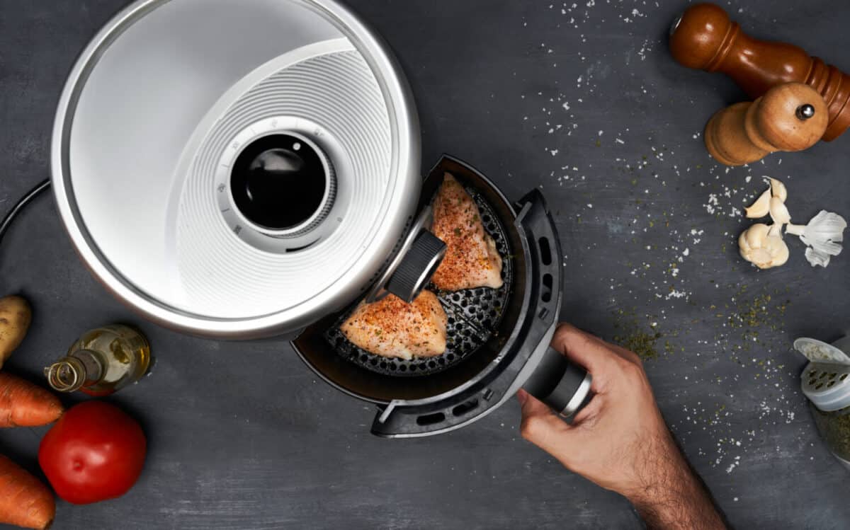 Unrecognizable man hand cooking skinless chicken breast with spices in an air fryer