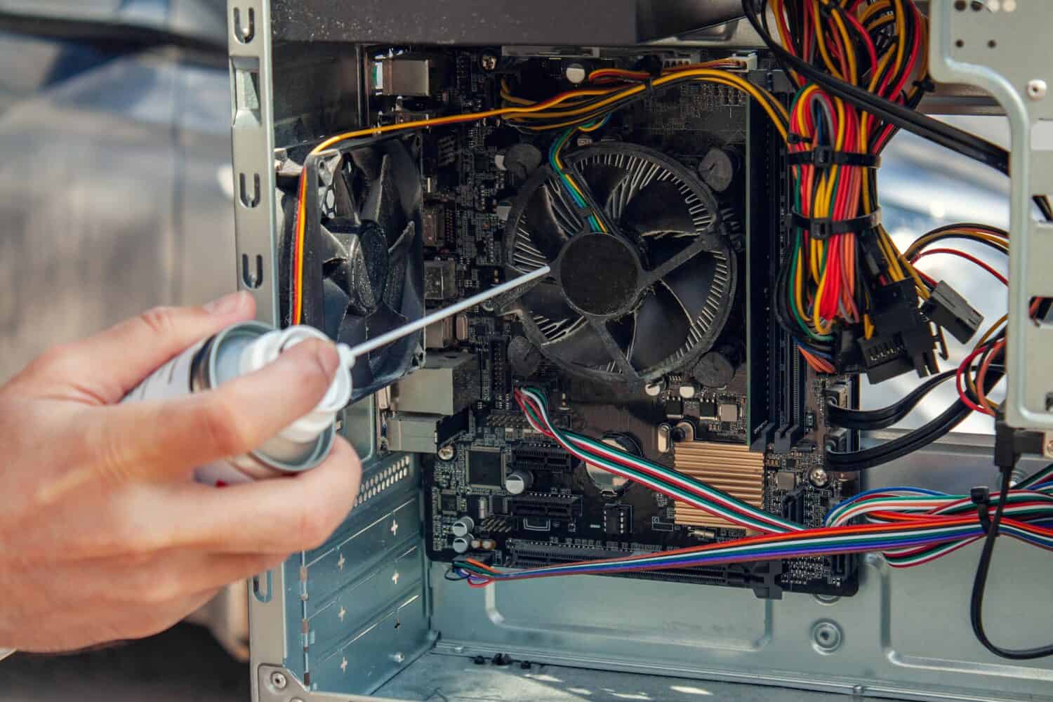 Maintenance and cleaning of the insides of the computer. Man's hand holds a cylinder of compressed air and cleans the insides of the computer.
