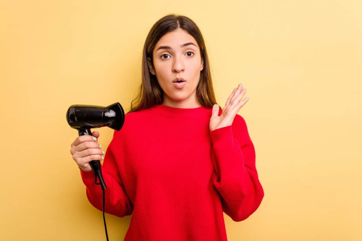 Young caucasian woman holding hairdryer isolated on yellow background surprised and shocked.