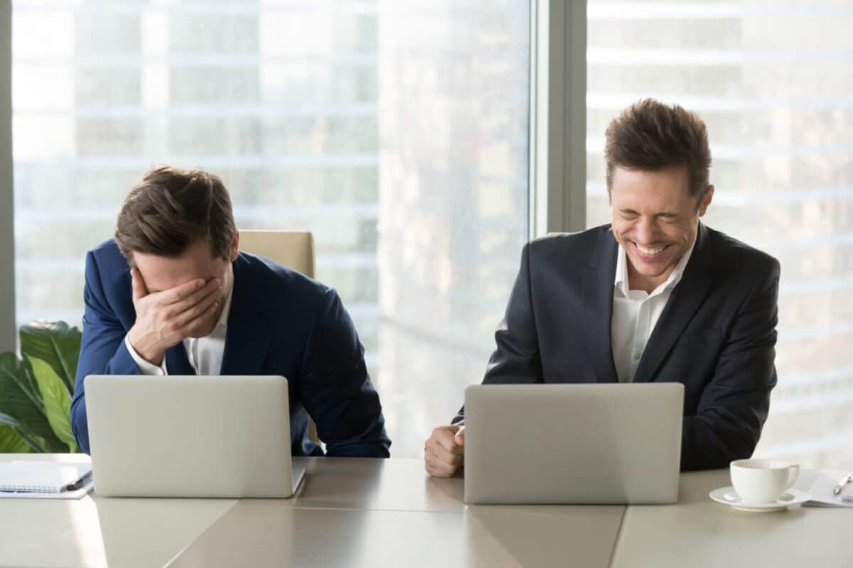 Two businessmen laughing out loud at workplace, office workers screaming with laughter and can not stop, funny positive emotions at work, cheerful colleagues having fun sitting at desk with laptops