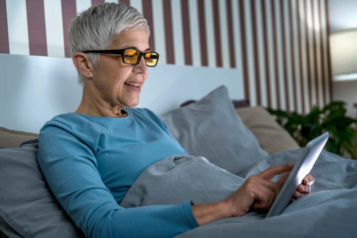 woman using blue light glasses in bed on tablet phone