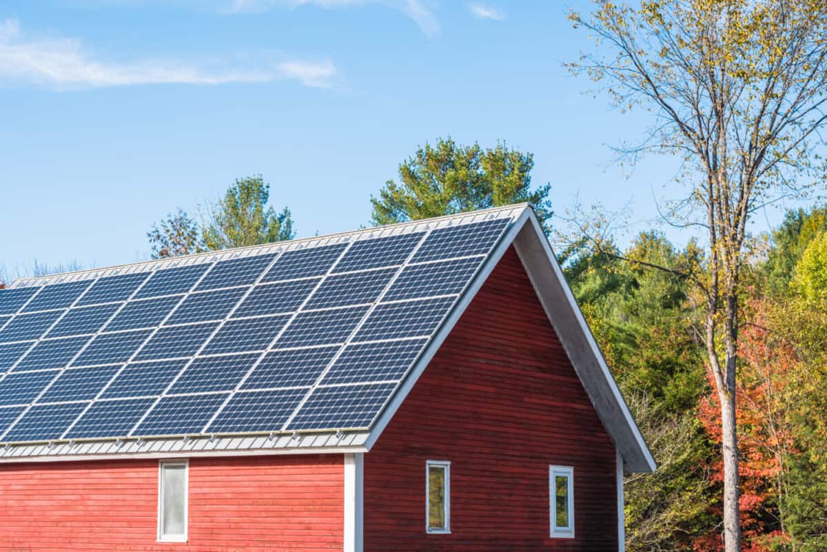 Solar panels for electricity generation on the roof of a traditional red wooden barn on a sunny autumn day. Countryside of Vermont, USA.