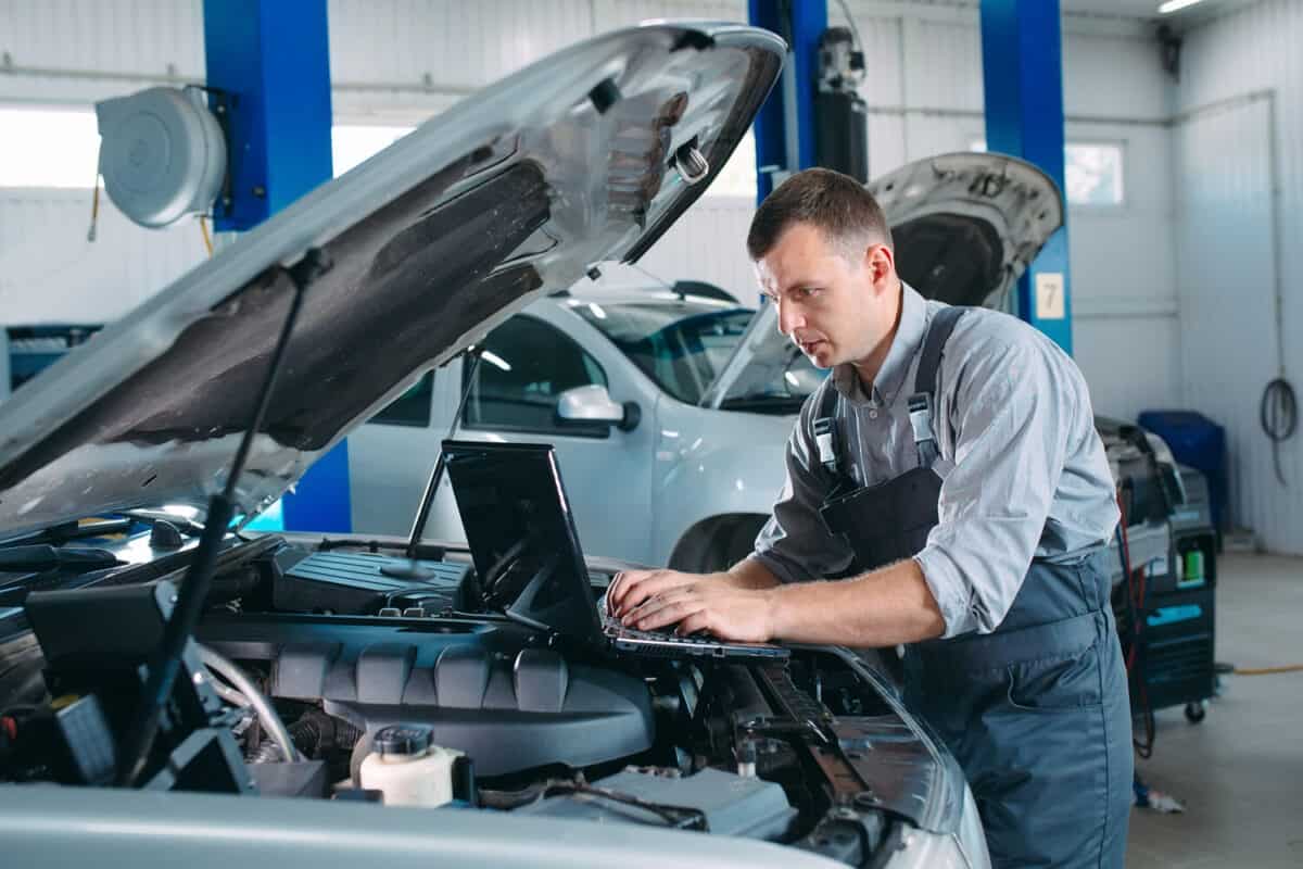 car mechanic using a computer laptop to diagnosing and checking up on car engines parts for fixing and repair