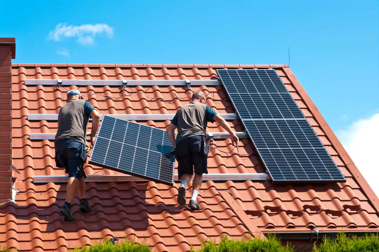 Two men installing new solar panels on the roof of a private house.