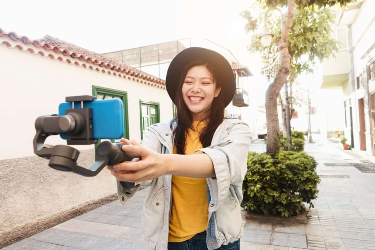 Happy asian influencer having fun vlogging with gimbal and mobile phone outdoor - Focus on face