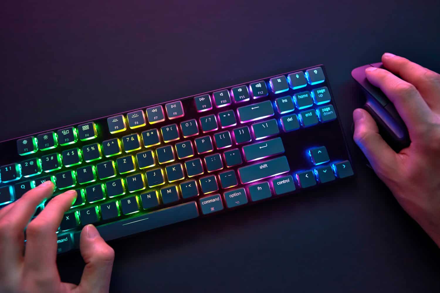Personal point of view on player hands using color backlighted keyboard and mouse. Professional computer game playing, esport business and online world concept.