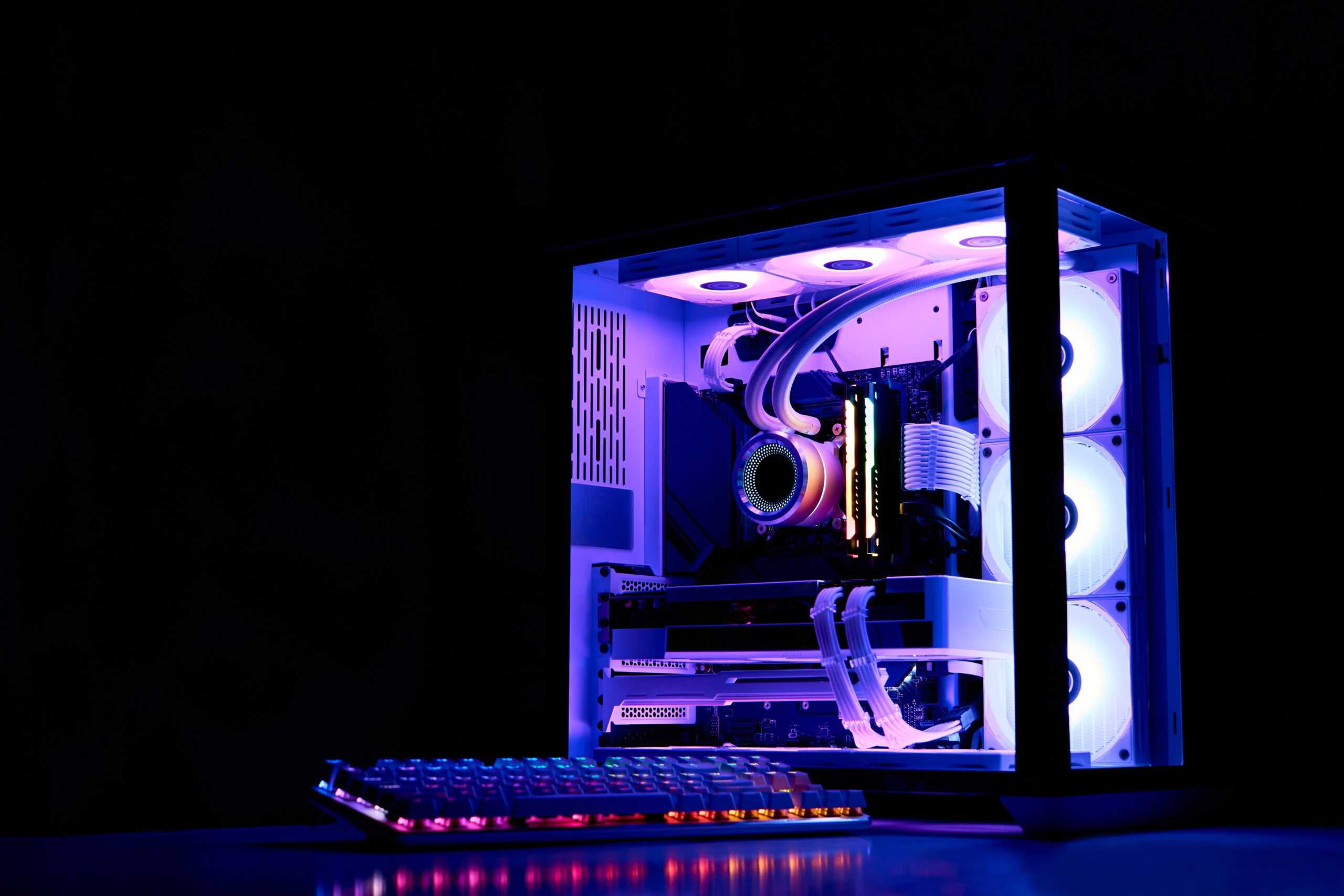 Gaming PC with rainbow LED light. Liquid cooled computer. Powerful PC in a glass case with keyboard. Gamer's workplace in a dark room, neon ligh