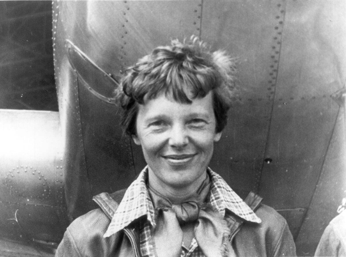 Photo of Amelia Earhart underneath the nose of her plane.