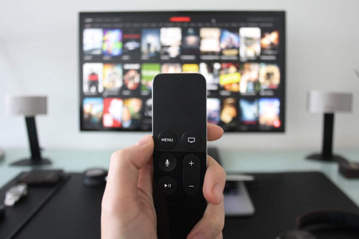 Hand holding a TV remote while watching shows on a streaming service on Television.