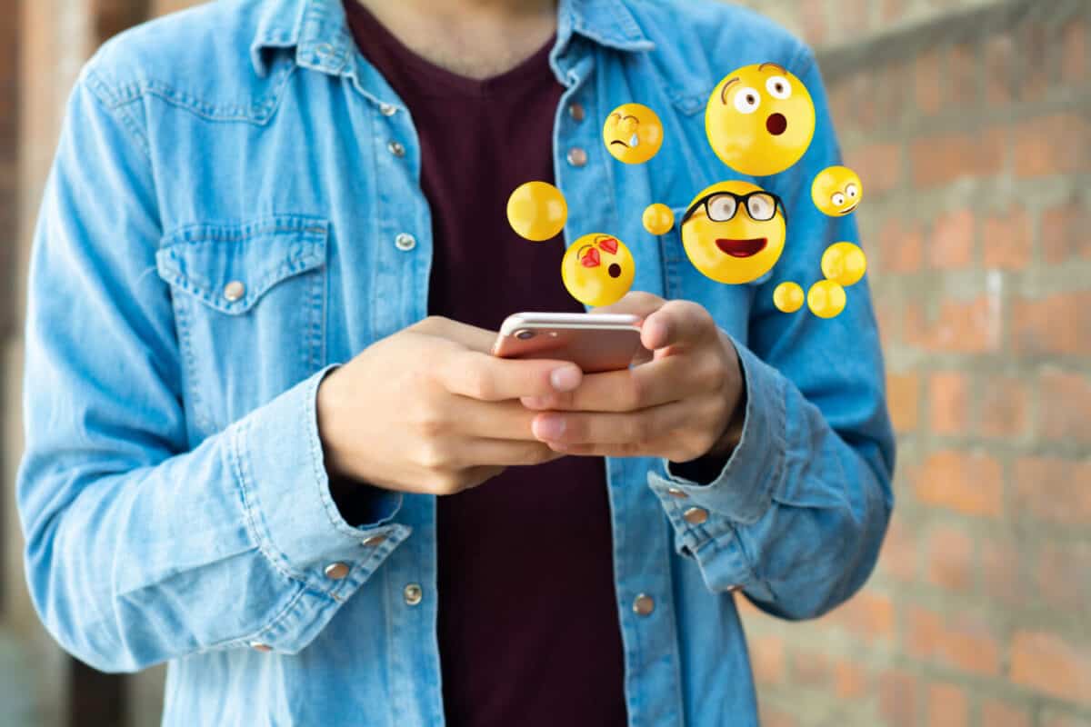 Close-up of man using smartphone sending emojis. Social concept.