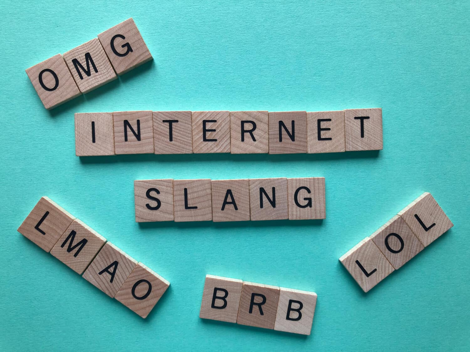 Internet slang. Acronyms : BRB (Be Right Back), LOL, OMG, and LMAO used as abbreviations in text messages, in wooden letters on a turquoise background with copy space.