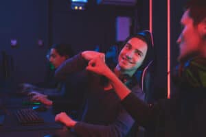 Team of computer gamers sitting at table and making fist bump while celebrating win in computer club