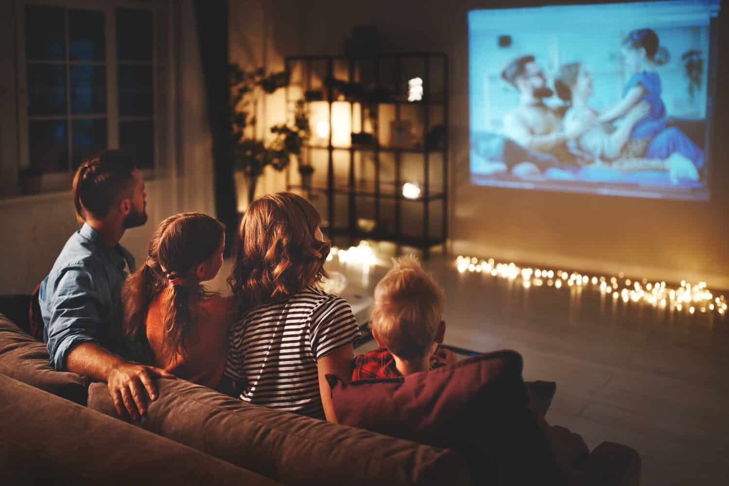 family mother father and children watching projector, TV, movies with popcorn in the evening at home