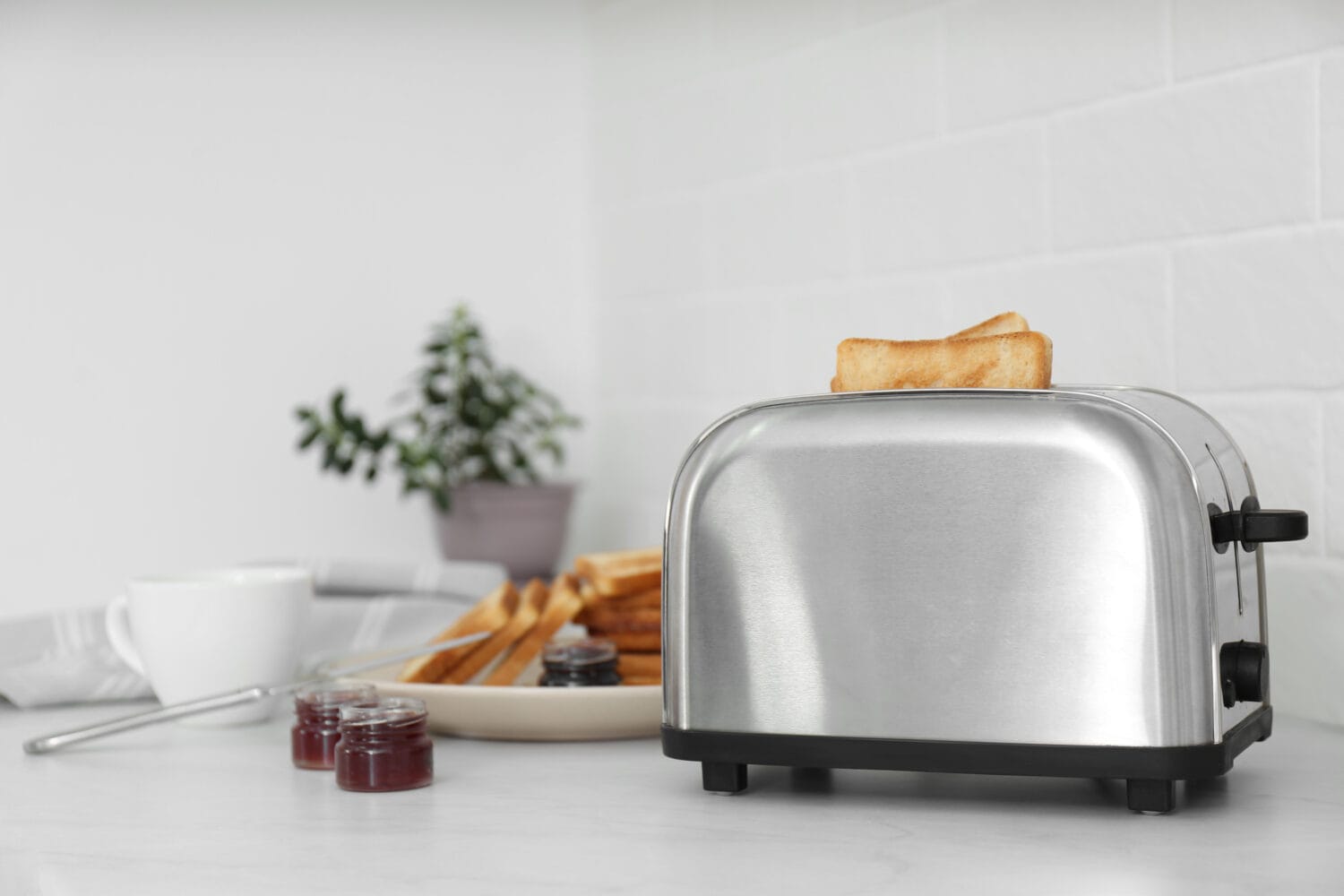 Modern toaster with slices of bread and different jams on white table in kitchen
