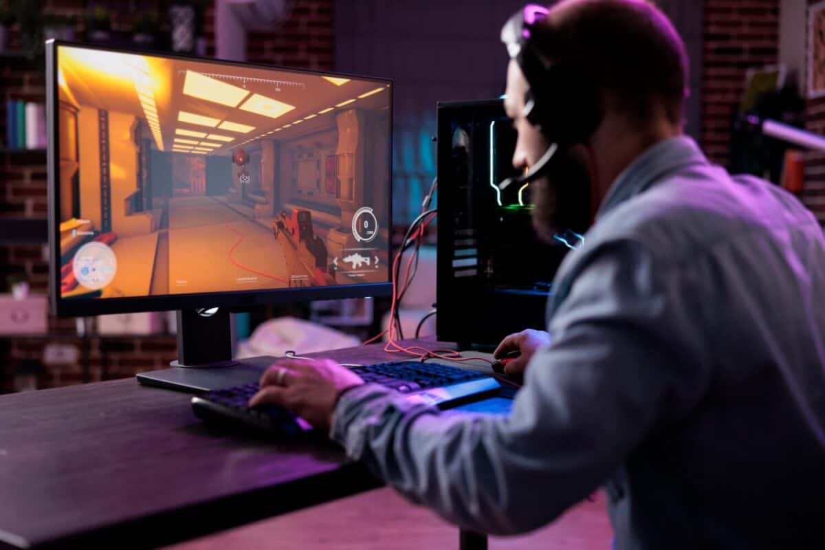 Male streamer playing online video games on computer, having fun with action gameplay tournament in space with neon lights. Young gamer enjoying gaming championship on webite.