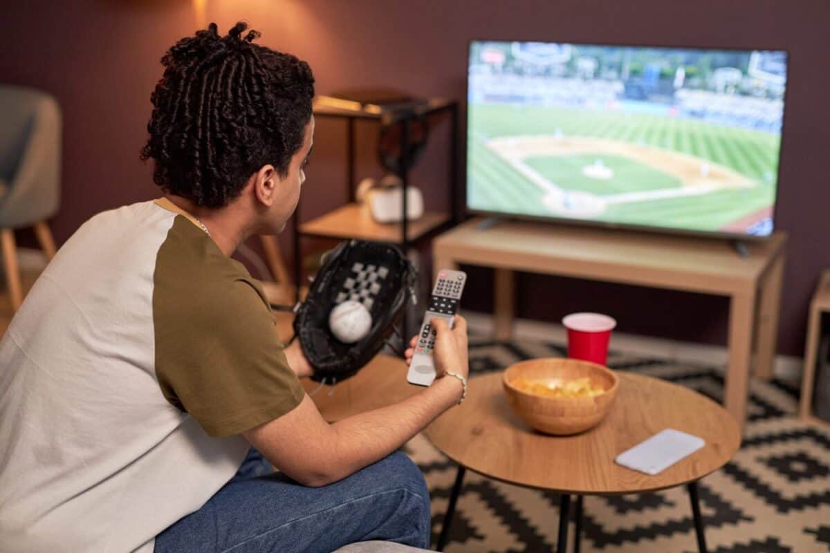 Side view portrait of baseball fan holding TV remote while watching match at home, copy space