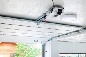 Opening door and automatic garage door opener electric engine gear mounted on ceiling with emergency cord. Double place empty garage interior with rolling entrance gate