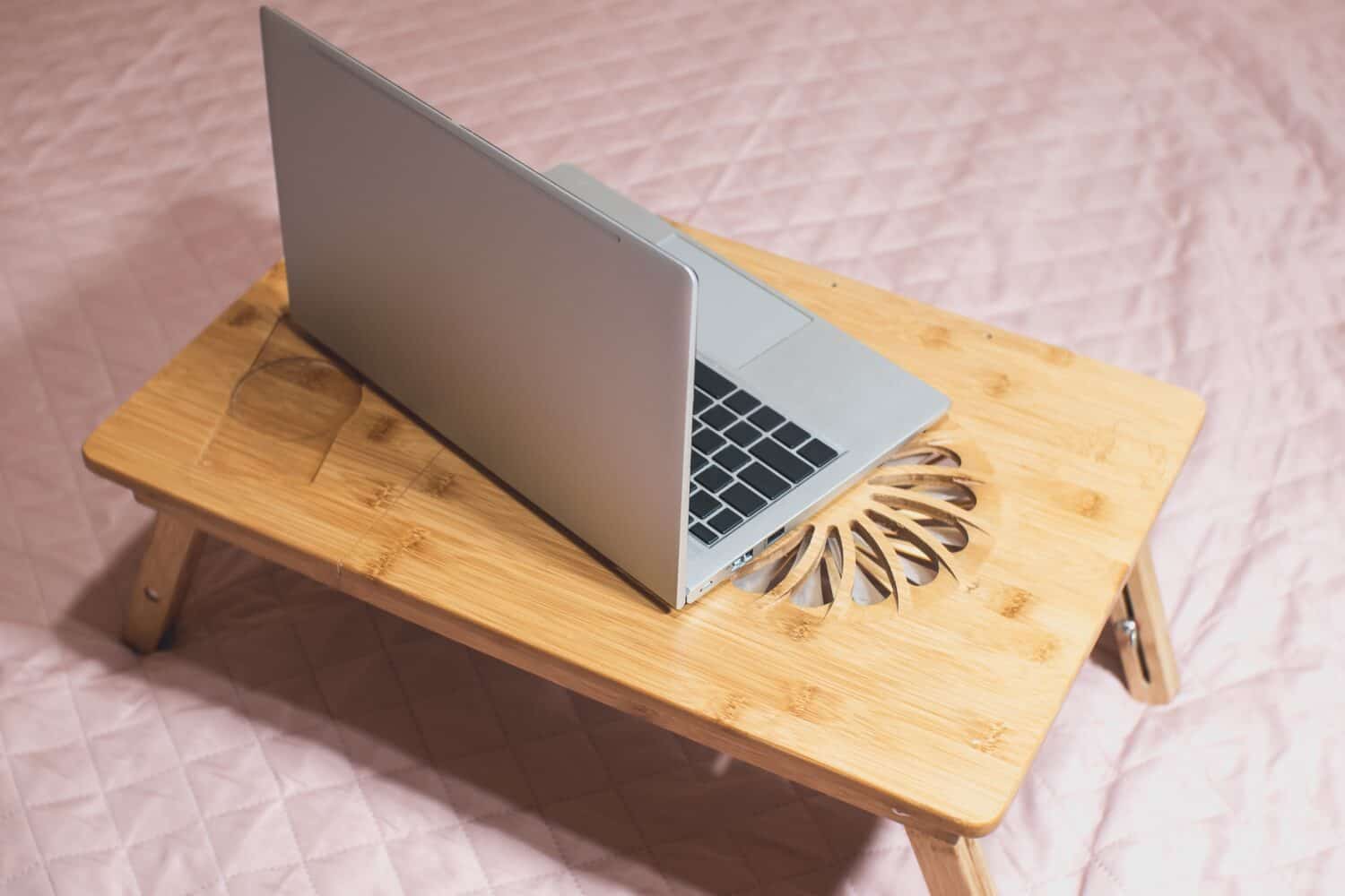 Modern gray thin laptop on the wooden Cooling pad for laptop. Notebook Cooler for Computer, USB Fan. Work with laptop on the bed.