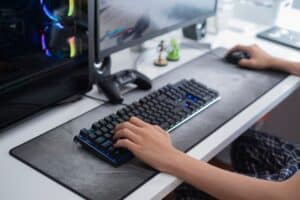 selective focus of a teenager hands playing on a gaming computer, with a black keyboard on a large gray mouse pad, addition to video games