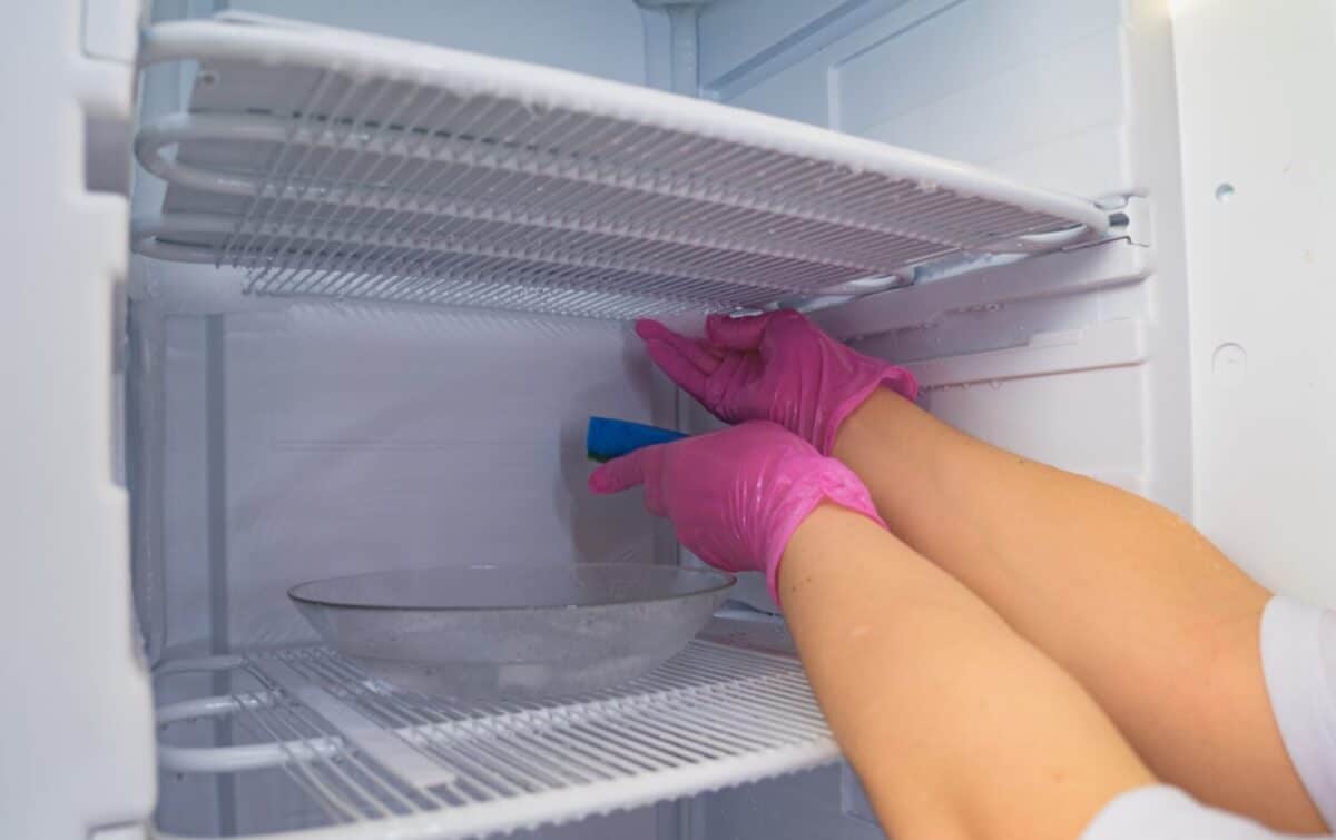 Defrosting and cleaning the freezer. A woman in latex gloves wipes meltwater with a sponge. Shallow depth of field.