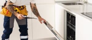 man repairing dishwasher. Male hand with screwdriver installs kitchen appliances, close up