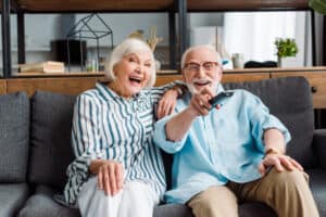 Senior couple laughing while watching tv on couch in living room