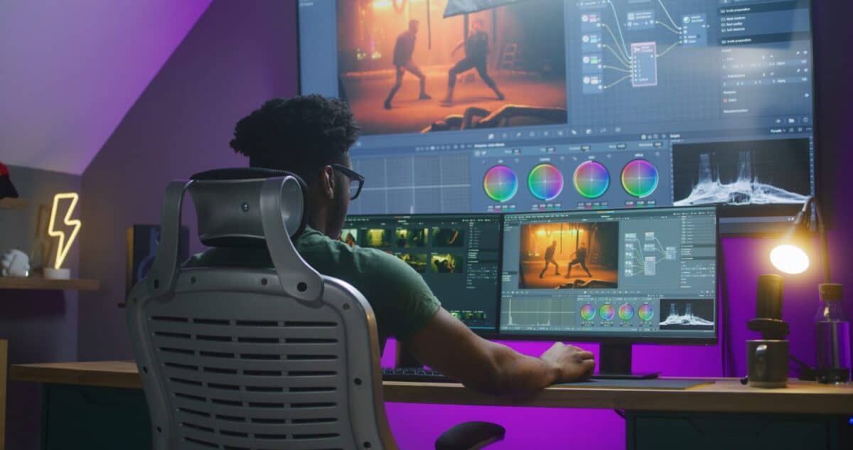 African American editor makes color correction, edits action movie, works at home. Software interface with RGB tools and wheels on computer and big digital screen. Concept of film post production.