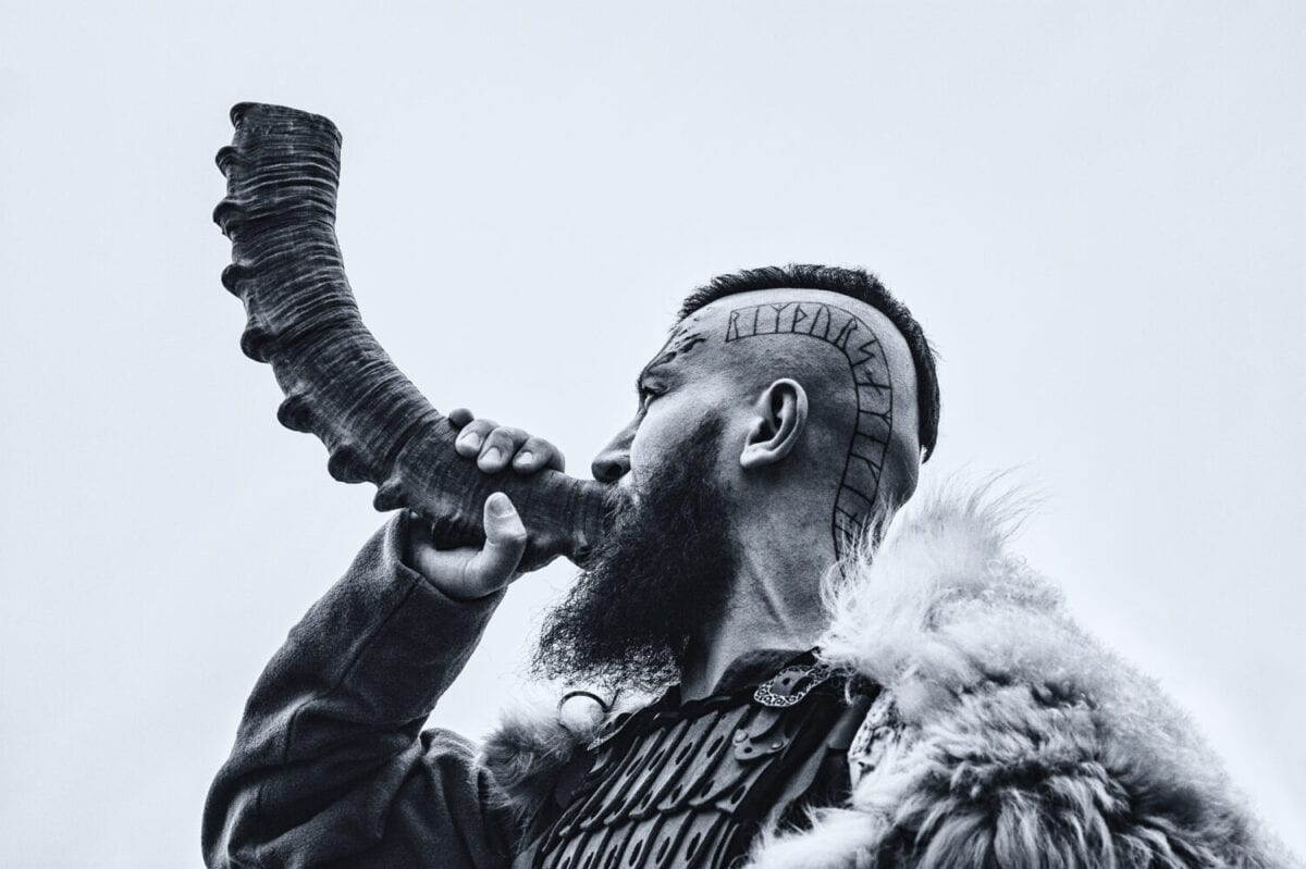 Brutal viking warrior blowing horn outdoors.